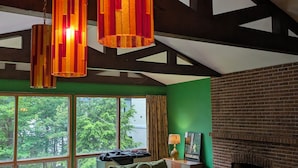 A living room with a fireplace, a sofa, a coffee table, and a view of trees through large windows.
