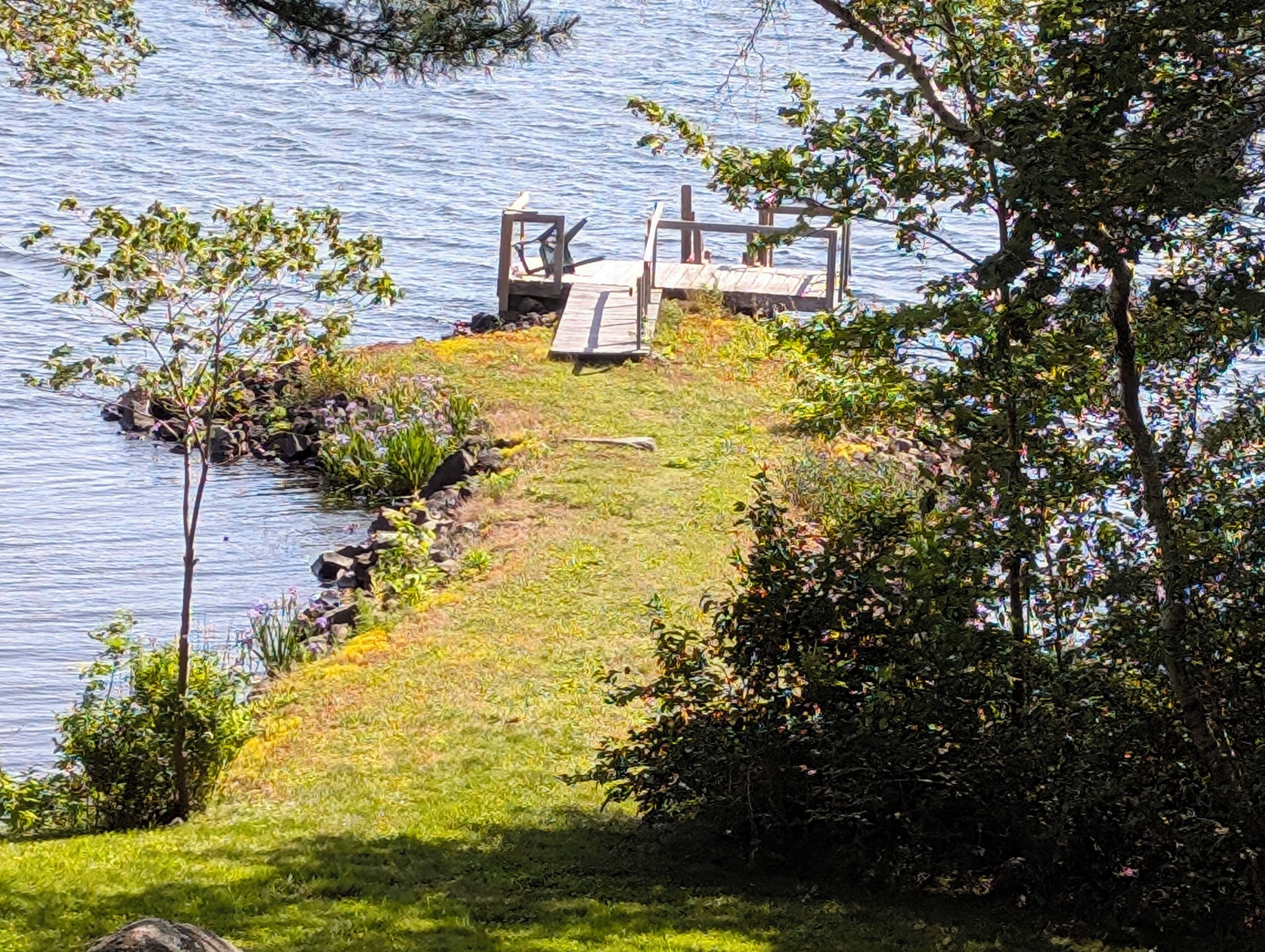 Een terras aan het meer met een houten constructie, omringd door gras en bomen.