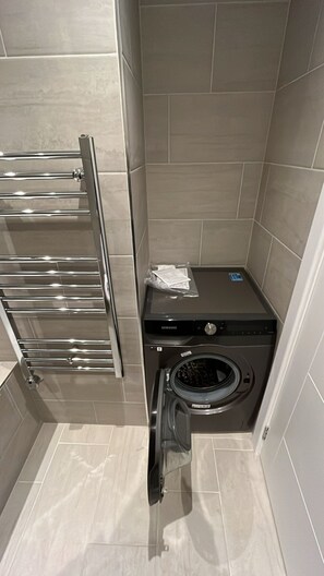 A compact bathroom with a stainless steel towel rack, a Samsung washing machine, and a small tiled wall. - Spacious Flat (ground floor) in Lambeth with gated parking (London)