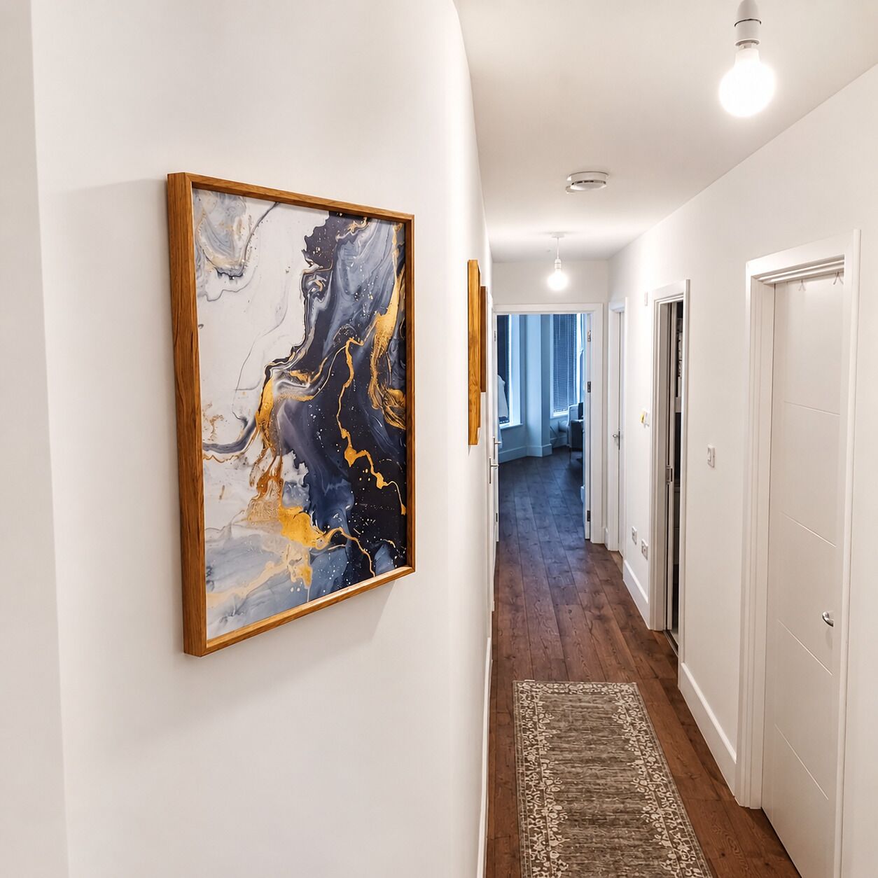 Un pasillo con una obra de arte de mármol en la pared, suelo de madera y puertas blancas.