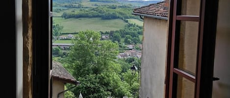 Une pièce dotée d’une grande fenêtre donnant sur un village et des collines verdoyantes.