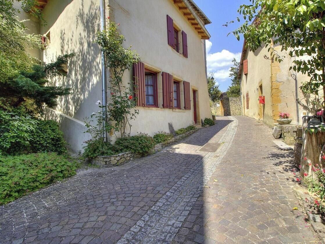 A narrow cobblestone street flanked by buildings with red shutters and stone walls.