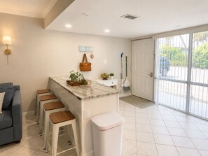A kitchen with a marble countertop, bar stools, a white toilet, and a grey sofa. - Coastal Retreat located on Manasota Key, Heated Pool, Beach & Bay Access (Englewood)