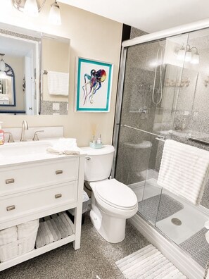 A modern bathroom with a white vanity, a toilet, a glass shower enclosure, and a framed artwork on the wall. - Coastal Retreat located on Manasota Key, Heated Pool, Beach & Bay Access (Englewood)