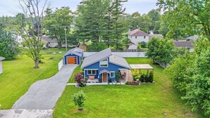 A residential house with a blue exterior, a front porch, and a driveway leading to the garage. - Indigo Hideaway | Romantic + Fire pit (Nappanee)