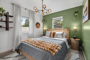 Een slaapkamer met een bed, een kroonluchter, een plant, een raam en een wandplank.
