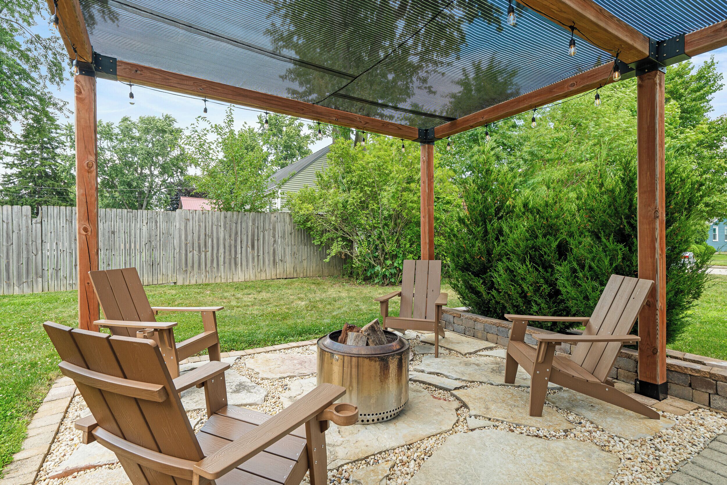 Een overdekt terras met houten stoelen en een vuurkuil.