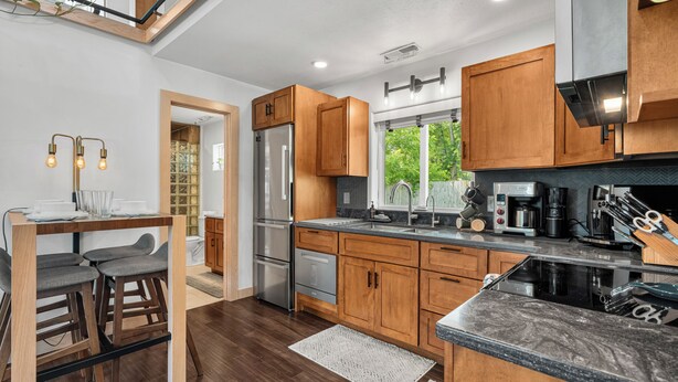A modern kitchen with wooden cabinets, stainless steel appliances, and a bar area with stools. - Indigo Hideaway | Romantic + Fire pit (Nappanee)