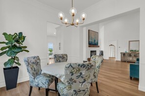 Ein Essbereich mit einer Kronleuchter, blumengemusterten Stühlen, einer großen Topfpflanze und Blick zum Esszimmer.