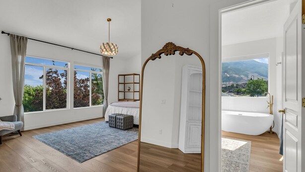 A bedroom with a large window, a bed, a mirror, and a view of the outdoors. - Remodeled 4BDR Home with Valley Views & Hot Tub (Draper)
