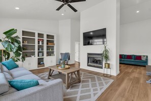 Ein modernes Wohnzimmer mit einer Couch, einem Couchtisch, einem Kamin, einem an der Wand befestigten Fernseher und einem Deckenventilator.