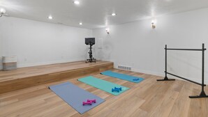 A room with wooden flooring, exercise mats, dumbbells, a TV on a stand, and a black exercise bar. - Remodeled 4BDR Home with Valley Views & Hot Tub (Draper)