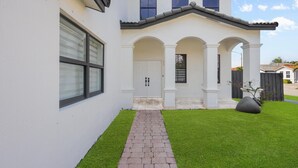 A two-story house with a white exterior, a brick pathway leading to the front door, and a well-maintained lawn. - La Cubanita (Miami)