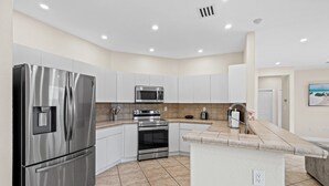 A modern kitchen with stainless steel appliances, white cabinetry, and a tiled backsplash. - La Cubanita (Miami)