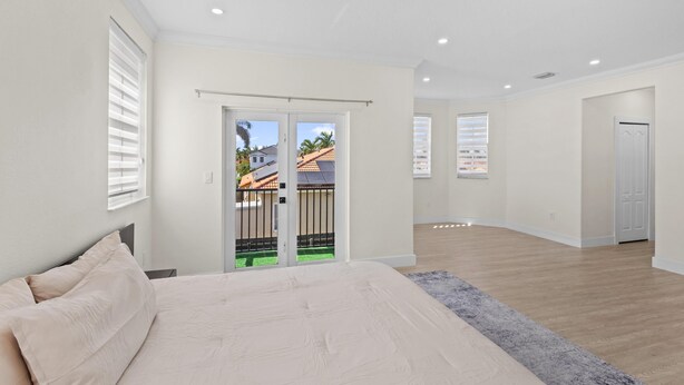 A bedroom with a bed, a sliding door to a balcony, and a view of a house. - La Cubanita (Miami)
