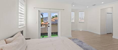 A bedroom with a bed, a sliding door to a balcony, and a view of a house.