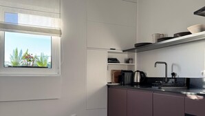 A modern kitchen with built-in appliances, a window with blinds, and a patterned rug. - Cosy Studio | Custom Tiles & Balcony · Leiria (Leiria)