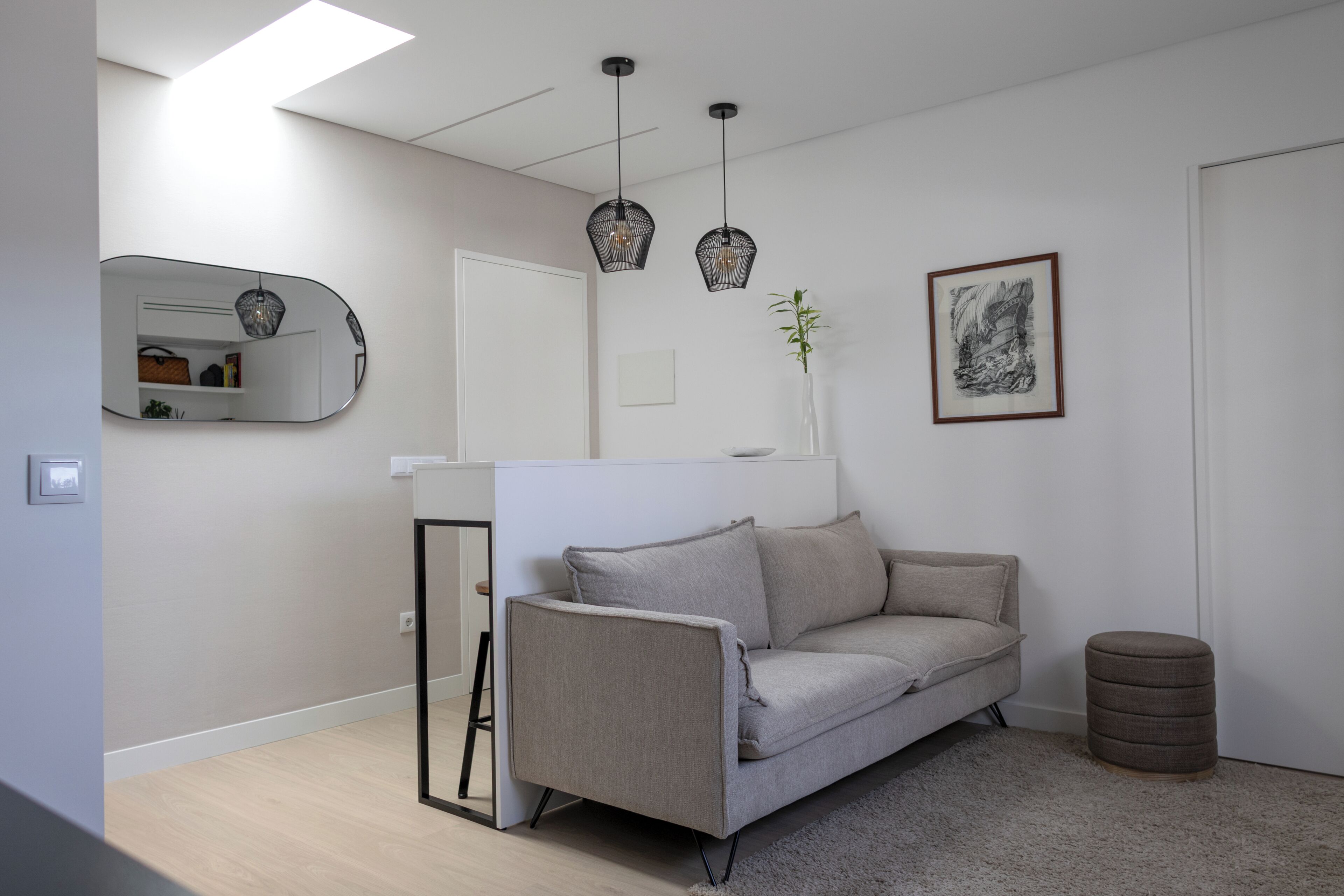 Una sala de estar moderna con un sofá, lámparas colgantes, un espejo y una obra de arte enmarcada.