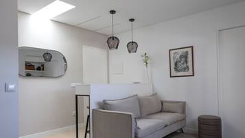 Una sala de estar moderna con un sofá, lámparas colgantes, un espejo y una obra de arte enmarcada.