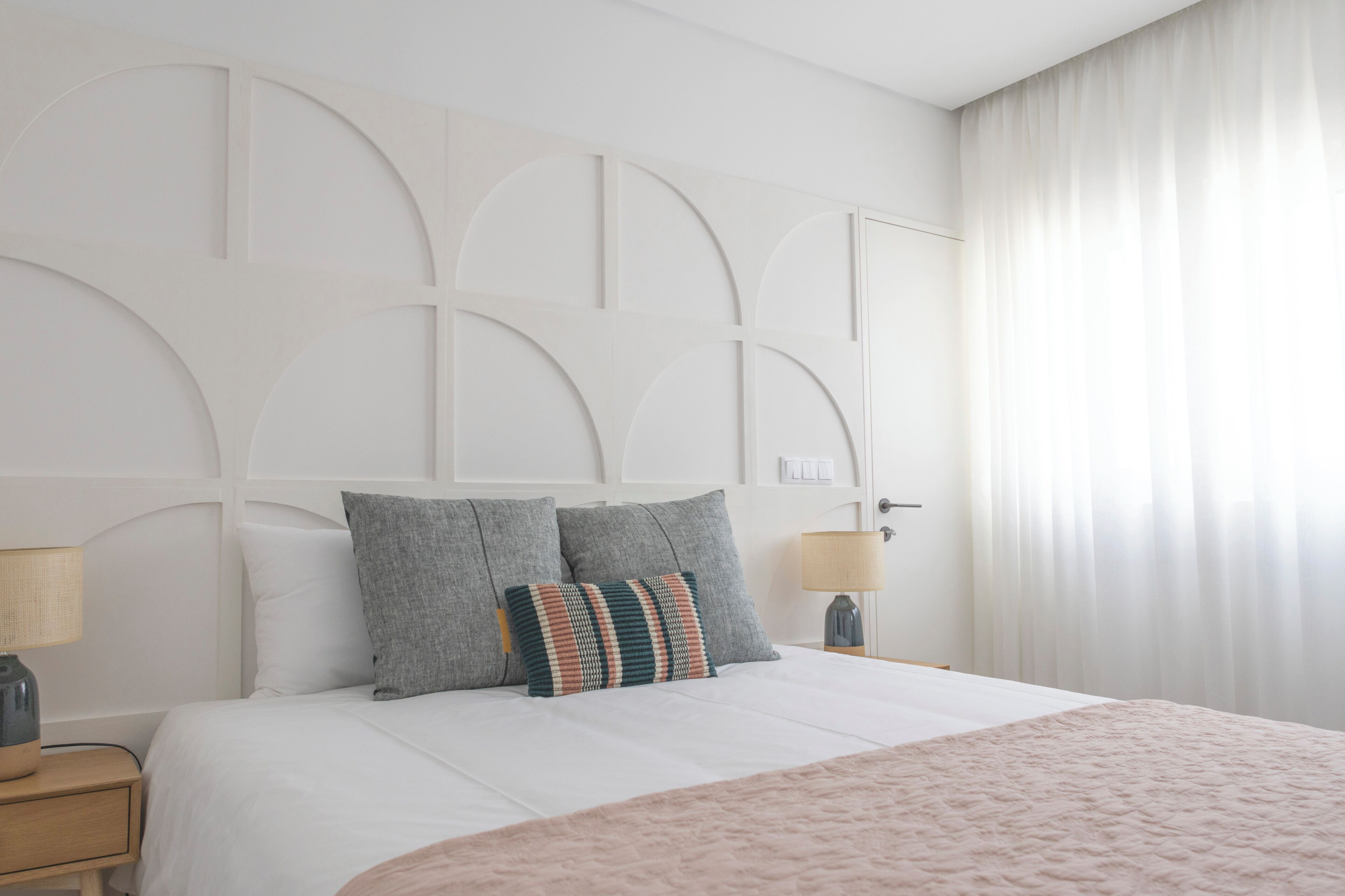 Habitación de hotel con cama, dos lámparas de noche, una mesita de noche y un ventanal con cortinas.