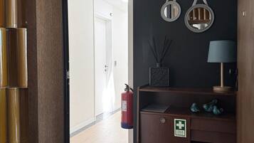 Un pasillo con piso a cuadros, un extintor, un botiquín y un estante con adornos.