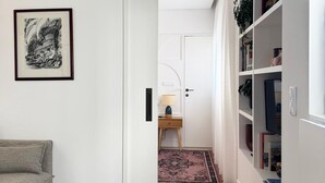 A hallway with a sofa, a framed picture, a bookshelf, and a door leading to another room. - Cosy Studio | Custom Tiles & Balcony · Leiria (Leiria)