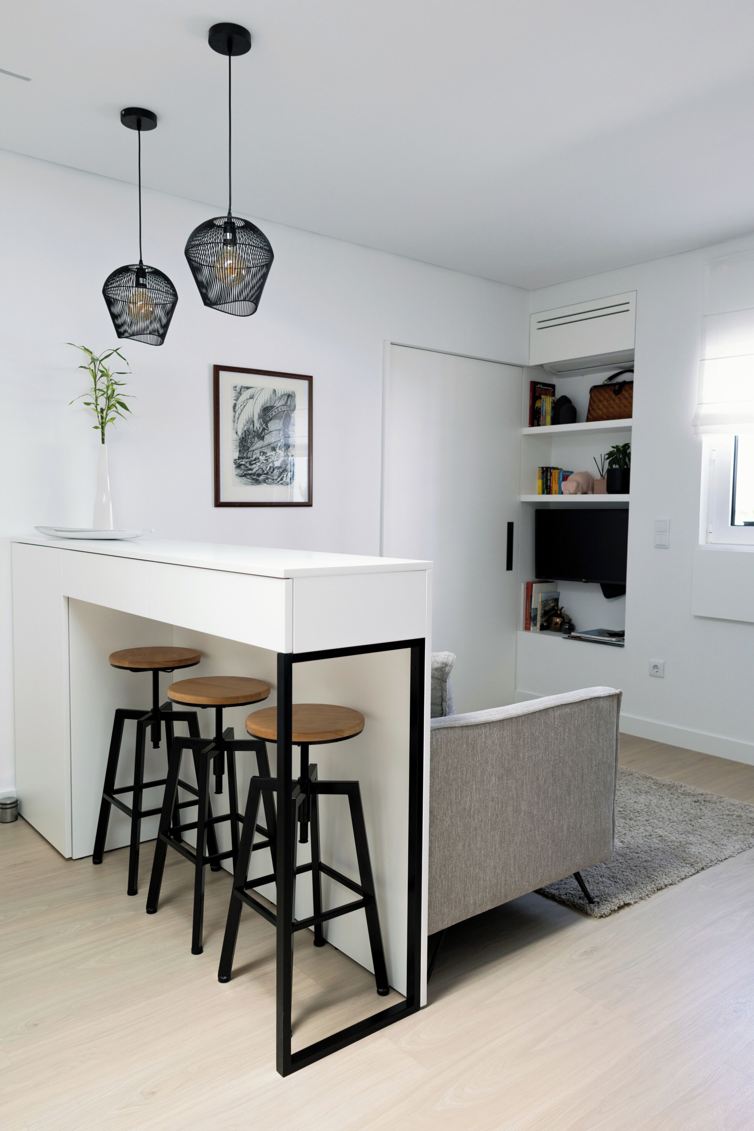A modern kitchen with a white countertop, three stools, pendant lights, and a grey chair.