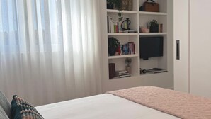 A bedroom with a bed, a bookshelf, a TV, and a window with curtains. - Cosy Studio | Custom Tiles & Balcony · Leiria (Leiria)