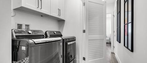 A laundry room with two front-loading washers and dryers, white cabinets above, and a door leading to another room.