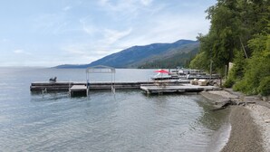 A lakeside dock with boats, a covered area, and a forested hillside in the background.