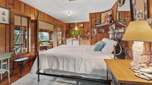A wooden cabin interior with a bed, a table, a chair, and a kitchen area.