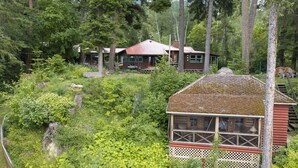 A cabin surrounded by dense forest, with a wooden deck and a small porch.