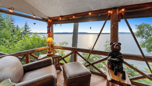 Eine Holzterrasse mit Seeblick, einer Bärenskulptur und einem Tisch mit Tassen.