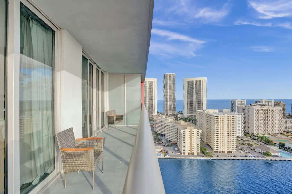 A balcony with wicker chairs, overlooking a cityscape and a body of water.