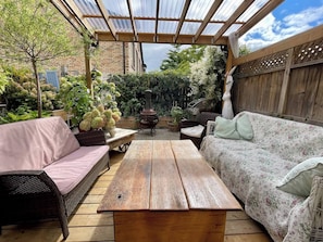 An outdoor patio with a wooden table, wicker sofa, and a covered seating area with a view of a brick building and greenery. - Room-french Nest, Private Bathroom! Chec (Burlington)