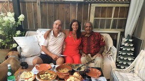 A group of people sitting on a couch with a table of food and drinks in front of them.