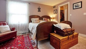 A bedroom with a bed, a chest of drawers, a red sofa, a window with sheer curtains, and a red patterned rug.