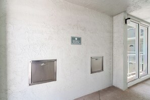 A hallway with textured walls, a trash can, and a sliding glass door leading to a balcony. - Martinique South 207 (Holmes Beach)