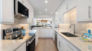 A modern kitchen with white cabinets, stainless steel appliances, and a central island. - Martinique South Unit 207 by SeaBreeze Vacation (Holmes Beach)