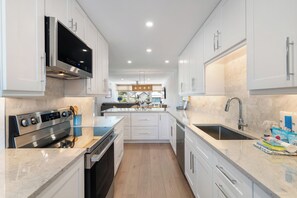 A modern kitchen with white cabinets, stainless steel appliances, and a central island. - Martinique South Unit 207 by SeaBreeze Vacation (Holmes Beach)