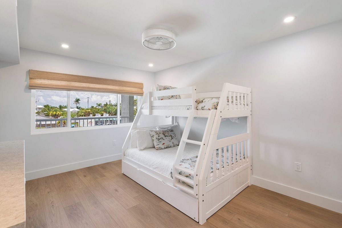 A bunk bed room with a window view, white walls, and a ceiling fan.