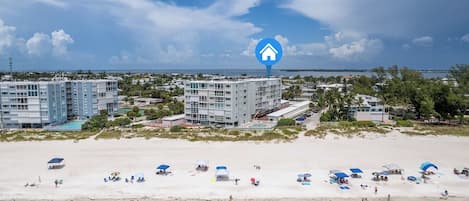 A beachfront hotel with multiple buildings, a sandy beach with umbrellas, and a clear view of the ocean.