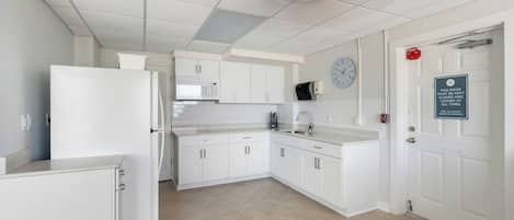 Una cocina moderna con armarios blancos, un microondas, un refrigerador y un reloj en la pared.