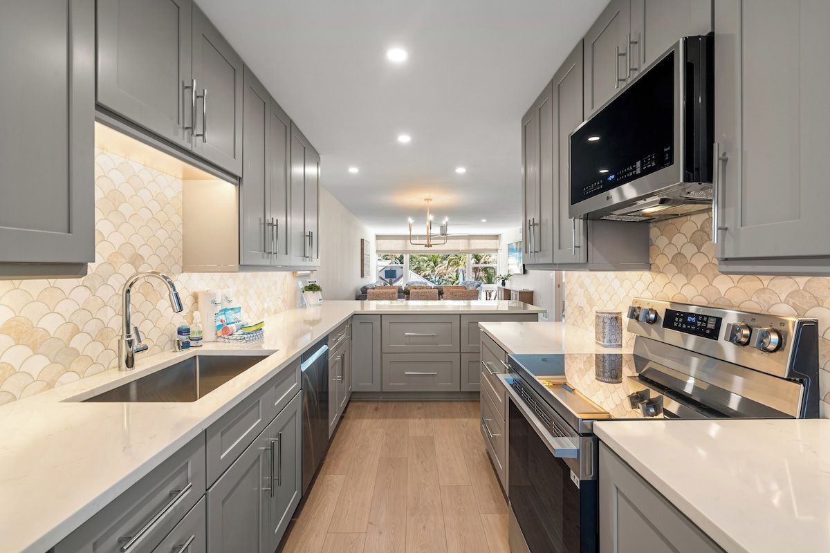 A modern kitchen with grey cabinets, a stainless steel range hood, and a large island with a sink.