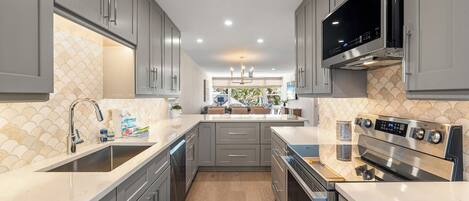 A modern kitchen with grey cabinets, a stainless steel range hood, and a large island with a sink.