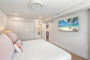 A bedroom with a bed, a wardrobe, a painting of a beach, and a ceiling fan. - Martinique South 306 (Holmes Beach)