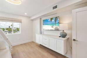 A modern hotel room with a large window, a flat-screen TV mounted above a white cabinet, and a staircase leading to an upper level. - Martinique South 306 (Holmes Beach)