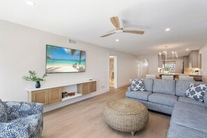 A modern living room with a flat-screen TV, a ceiling fan, and a large window with a beach view. - Martinique South 306 (Holmes Beach)