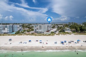 A beachfront hotel with multiple buildings, a sandy beach with umbrellas, and a clear view of the ocean. - Martinique South 306 (Holmes Beach)
