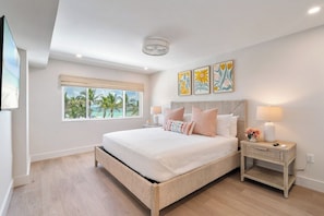 A bedroom with a large bed, a bedside table, a window with a view, and artwork on the wall. - Martinique South 306 (Holmes Beach)